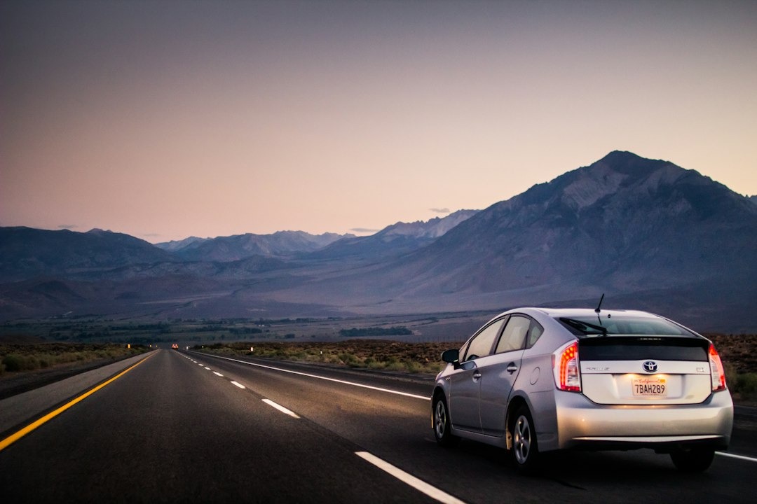 Silver Toyota Prius drives down a highway towards mountains at dusk.